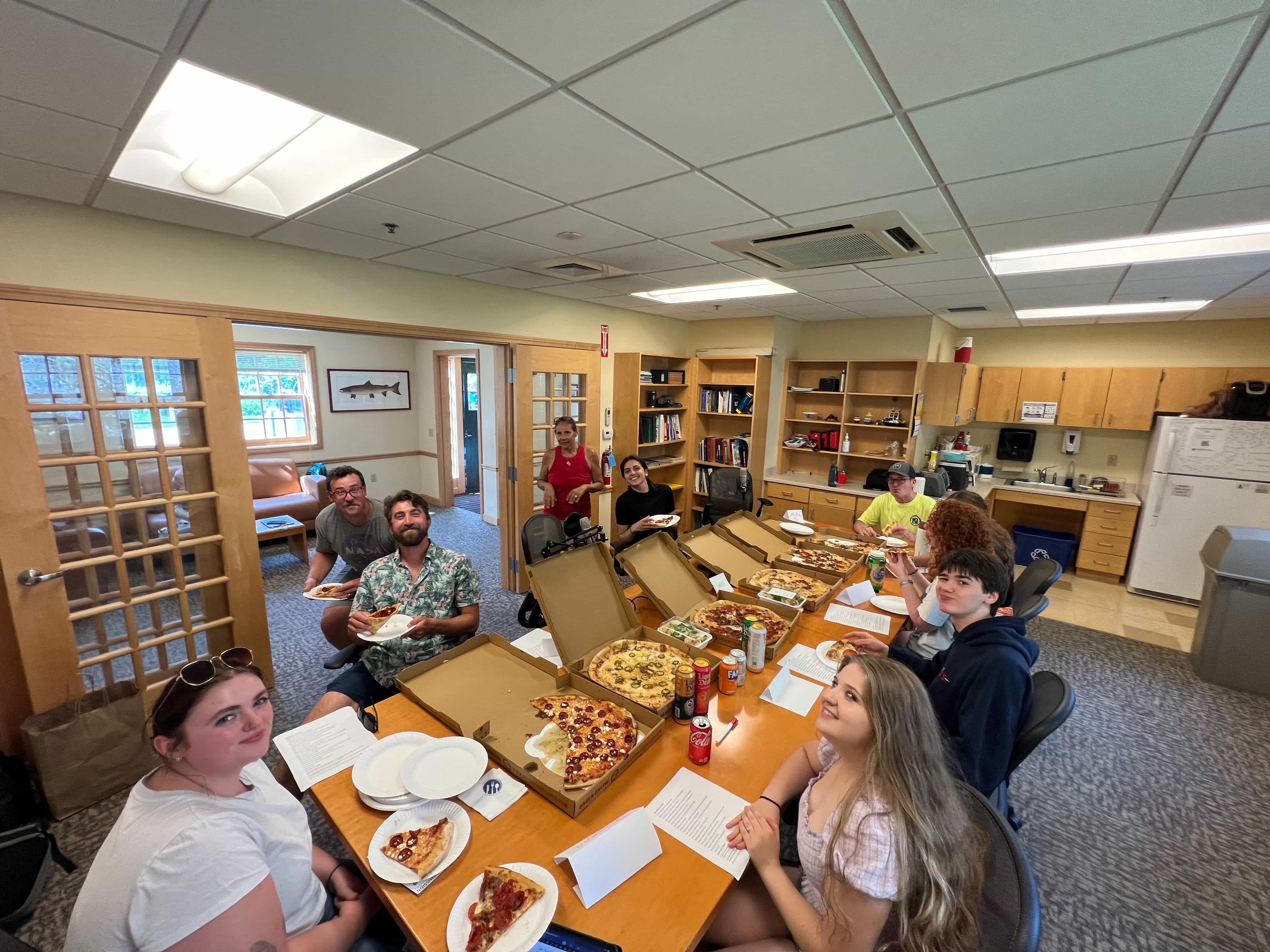 People gathered around a table with pizzas