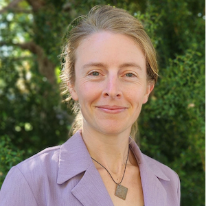 Dawn Harfmann stands outside in a lavender button up shirt and a pendant necklace