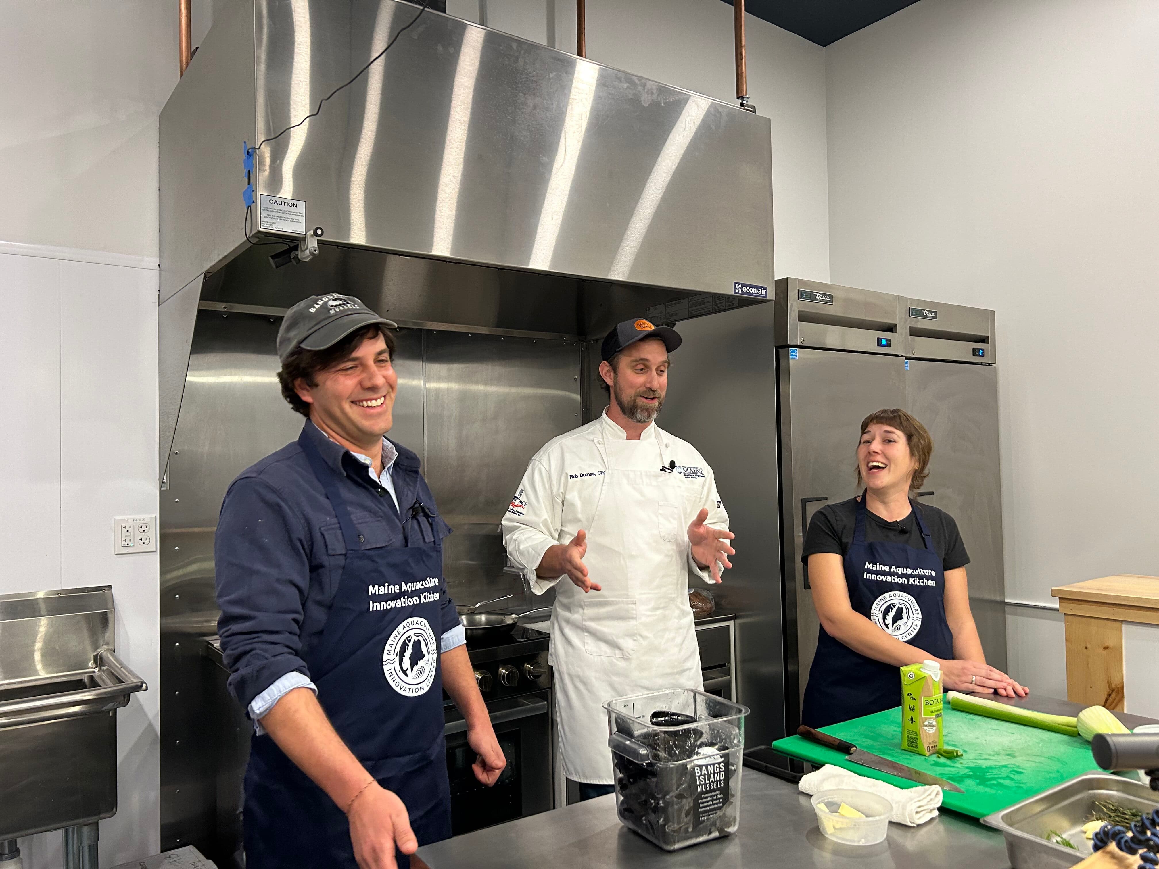 Chef Rob Dumas (center) cracks a joke that has Matt Moretti of Bangs Island Mussels, and Emily of MAIC, laughing while learning to cook Mussels Gratin