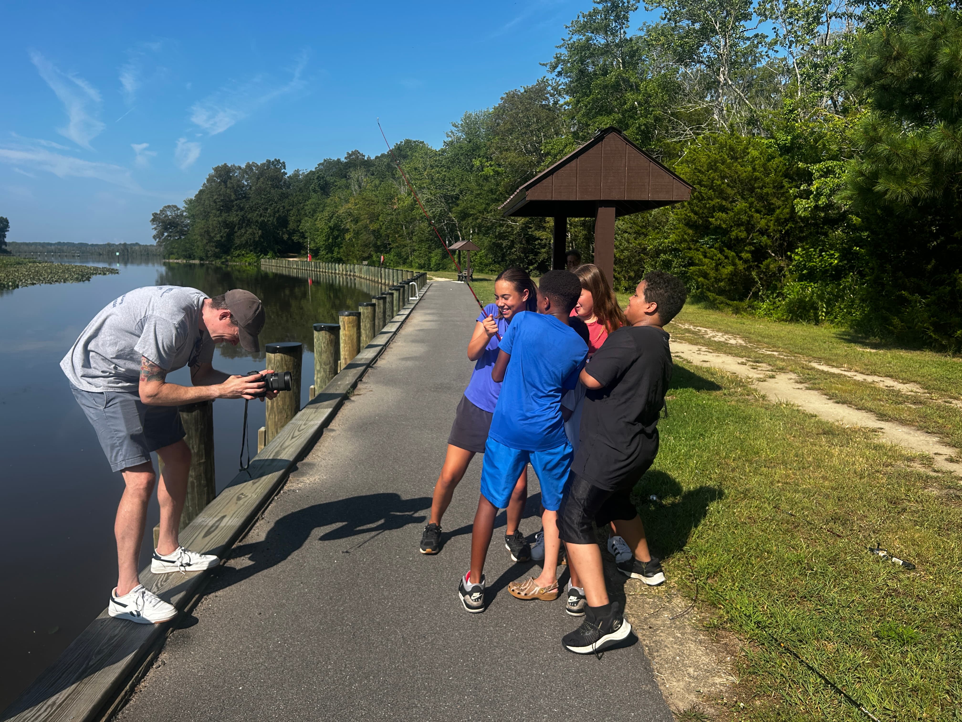 Kids pull fishing rod by lake while filmmaker films