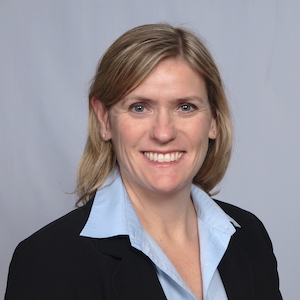 Photo of Sarah Bodor who has blonde shoulder-length hair and wears a blue button-up shirt, dark blazer. 