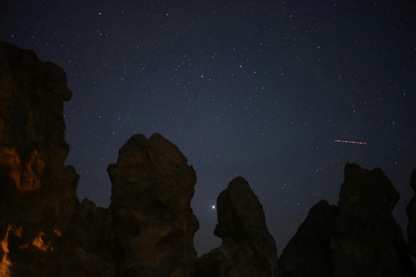 A night sky with stars and the silhouettes of rock formations in front of it