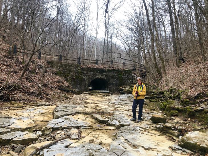 A hiker standing in front of a bridge on a dry creek bed