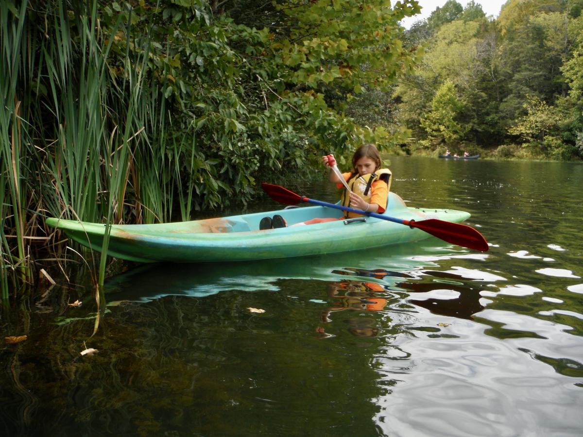 A young person gathering a water sample from a kayak.