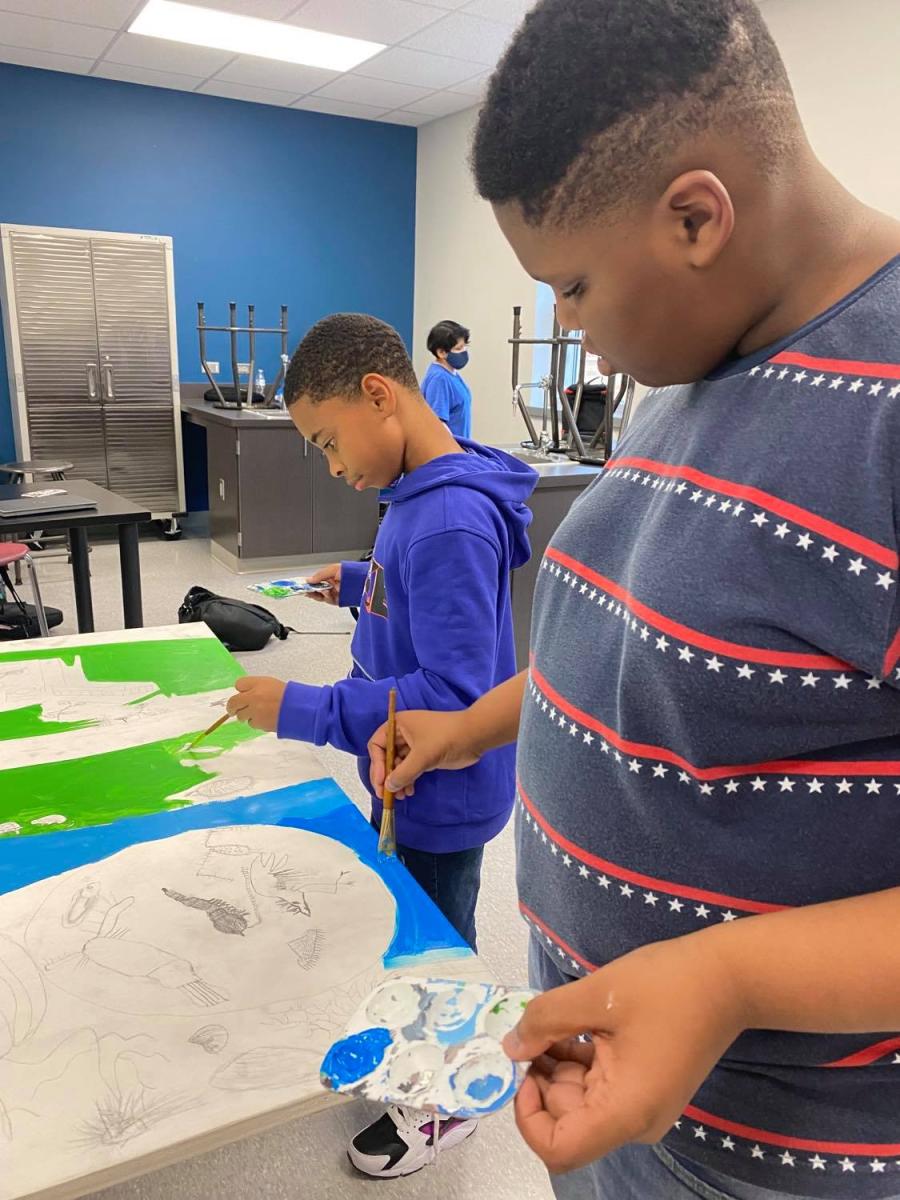 Two students stand at a desk to pain a mural