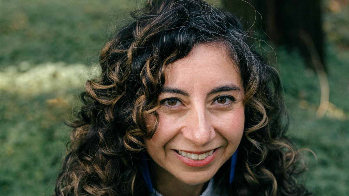 Kathayoon Khalil has long curly hair and stands outside surrounded by greenery