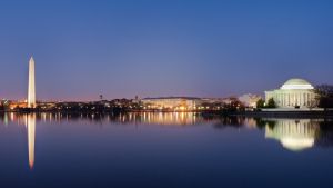 Washington DC at dusk. The Washington Memorial stands illuminated on the left. The Jefferson Memorial, also illuminated stands to the right. The river runs in the foreground. 