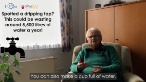 An elderly woman with short white hair, wearing a green sweater, sits in an armchair while talking to an off-camera interviewer. Text overlay shows logos for the H2Our Project and 5swaraj, with the text "Spotted a dripping tap? This could be wasting around 5,500 litres of water a year!"