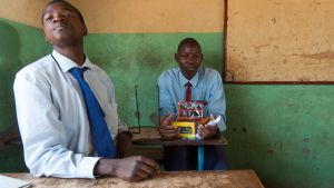 Two students in a classroom, one holds a mini solar panel while the other looks ahead