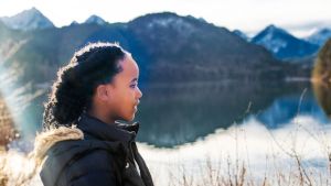 Profile of a Black child in front of a mountain lake on a partly cloudy day
