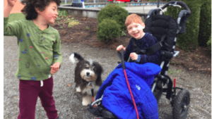 Two preschool kids one in a stroller play with a dog at nature-based inclusive preschool