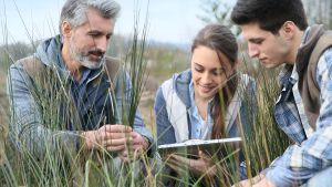 teacher with high school students looking at laptop in field