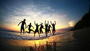 Friends jumping for joy on tropical beach at sunset in a group formation
