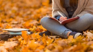 student sitting on autumn leaves writing in notepad