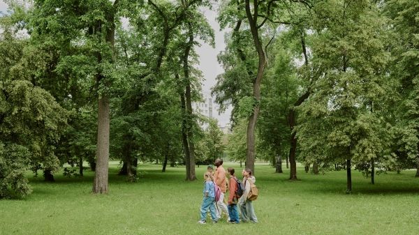 Teacher leading students carrying backpacks through green park