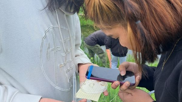 A student holds a cell phone over a card another student is holding.