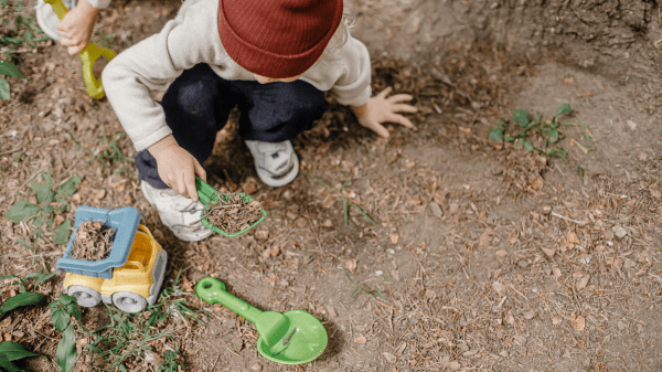 Early Childhood A child digs in the dirt with a green plastic shovel, below them is a plastic truck and another shovel