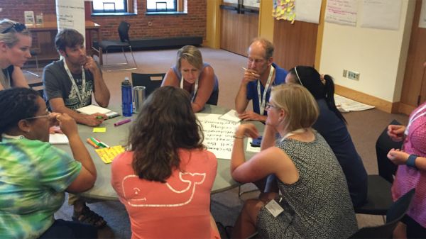 Climate Generation Short Course Group of adults with thoughtful expressions gathered around a round table with markers and chart paper.