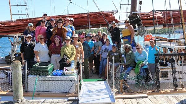 A group of teachers smile while sitting on the deck of a tall ship schooner.