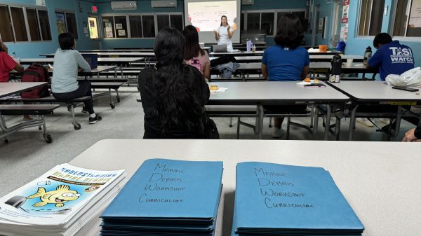 The Commonwealth of the Northern Mariana Islands Educator Workshop in July 2024 (Photo Credit: NOAA). A presenter is speaking to a classroom of people with a stack of marine debris curriculum workbooks piled on one of the desks.