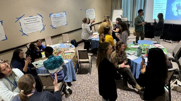 Photograph of several workshop participants interacting with each other in an indoor space with tables.