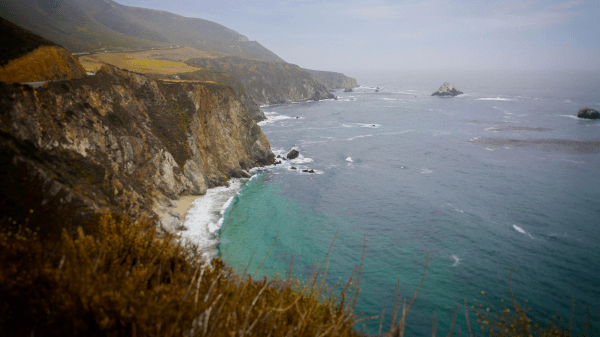 California Coast Coastal cliffs to the left of a blue ocean, a slightly cloudy blue skey behind them