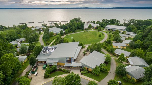NorthBay in North East, Maryland An aerial view of a campus with many gray-roofed buildings; trees and paths are interspersed between the buildings. In the background, a large body of water.