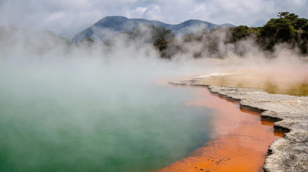 Earth Science A body of water covered in steam with mountains and sky in the background; the shore to the right has orange outlining it