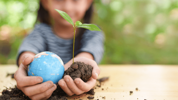 The Climate Initiative’s Resources for Educators Two hands of a child reach out over a table, in the right hand is a small globe, in the left some soil with a green sprout; behind this is the child blurred with a green background