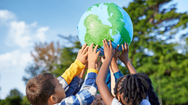 Youth Climate Summit A group of children hold up a paper mache globe above their heads; behind them is a partly cloudy sky and a blurred green tree