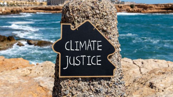 Climate Justice NEH K12 Institute A house-shaped chalkboard with the words "Climate Justice" on it hangs from a pole in front of a sandy beach and ocean