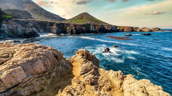 EARTH Lessons and Workshops A rocky outcropping lets out onto the ocean; behind it is a green hill and cloudy sky