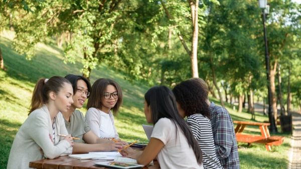 Image of multiethnic group of young students sitting and studying outdoors while talking.