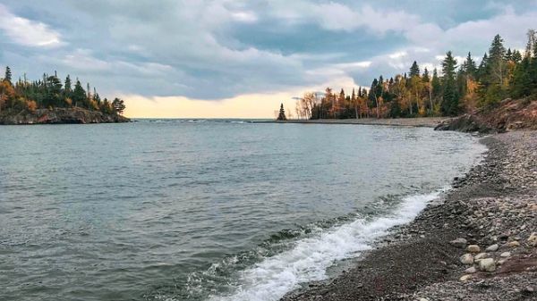A rocky lakeshore lined by trees in autumn