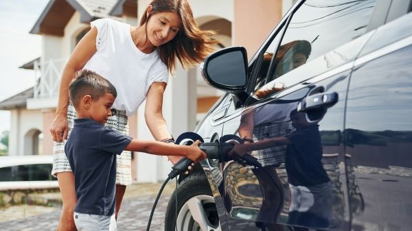 A woman and young boy plug in an electric vehicle 