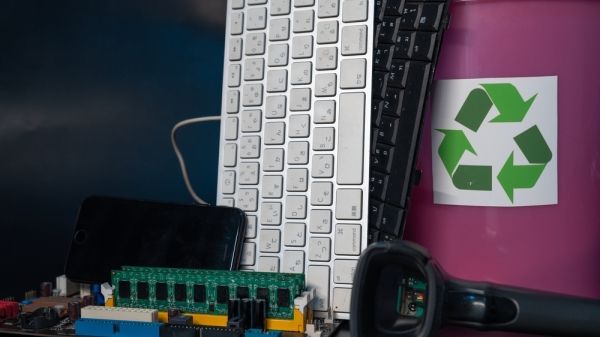 A keyboard, phone, headphones, and other electronics sit next to a recycle sign.