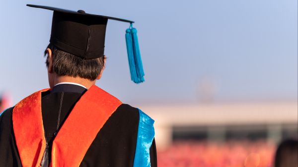 Master of Natural Resources A person to the left side of the image is wearing a graduation cap and gown; to the right of them is a blurred building and background