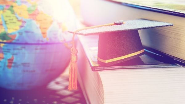 Black graduation cap on two big text books and a laptop