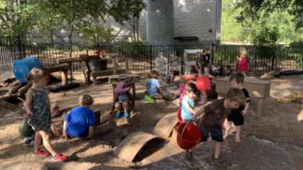 Young children playing in an outdoor sand and water area with a variety of loose parts