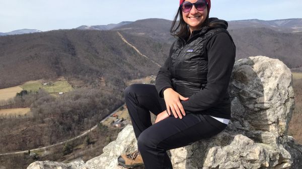 A smiling woman sitting on the edge of a high ridge
