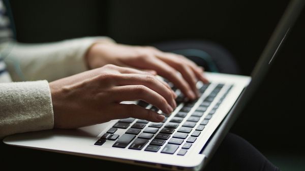 A person's hands hover over a laptop keyboard.