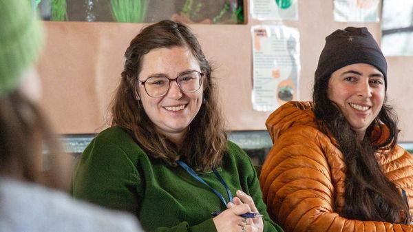 Two people in warm attire smile broadly at a person in the foreground.