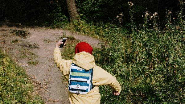 A child running on a dirt pathway while holding a phone