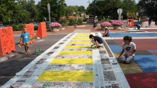 Photo of a group of four children kneeling or sitting while painting over a street