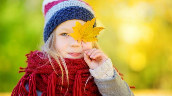 young girl holding a yellow autumn leaf in front of her eye