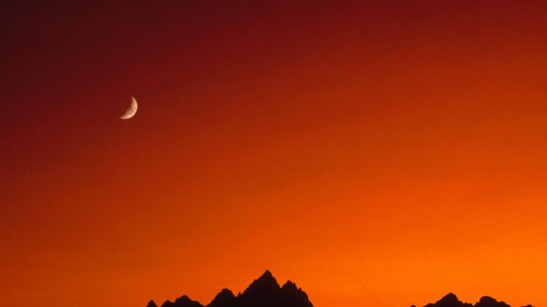 Reddish sky, moon, silhouette of mountains.