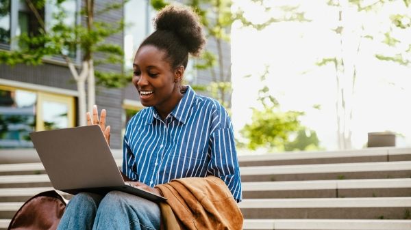 Person holding video conference with laptop and waving while sitting on stairs outdoor