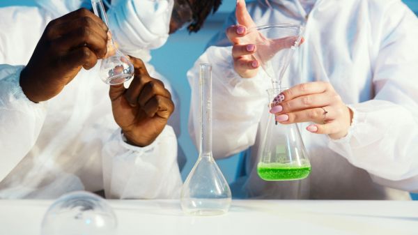 Zoomed in picture of two people in white lab coats holding test tubes and beakers over a white table
