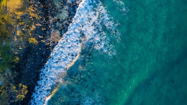 A breathtaking aerial view showcasing turquoise ocean waves crashing against a rocky shoreline.