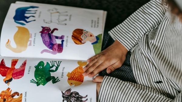 Child holding a picture book with pictures of colorful animals.
